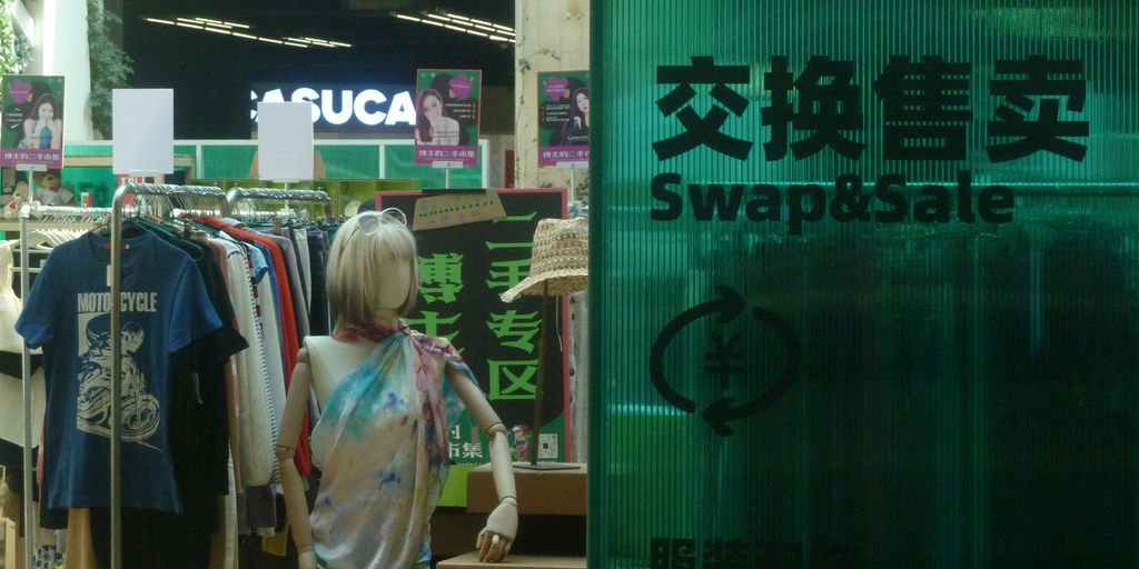 A mannequin stands near clothes for sale.